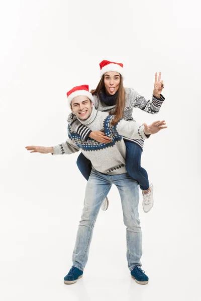 Boże Narodzenie koncepcja - młoda szczęśliwa para w swetry cieszyć piggyback jazdą na białym tle szarym tle — Zdjęcie stockowe