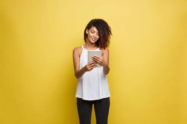 Lifestyle Concept - Retrato de la hermosa mujer afroamericana alegre leyendo algo en la tableta electrónica. Fondo amarillo pastel estudio. Copiar espacio . — Foto de Stock