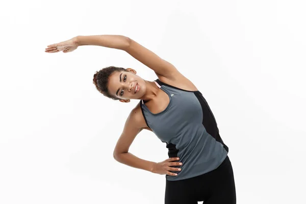 Sport, allenamento, stile di vita e concetto di fitness - ritratto di una bella donna afroamericana felice che si allunga le mani. isolato su sfondo bianco monolocale . — Foto Stock
