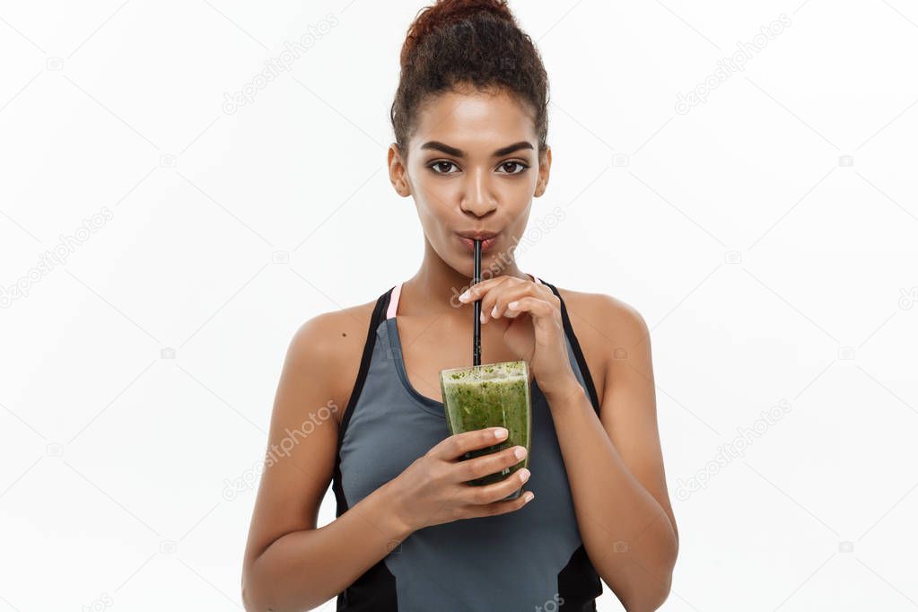 Healthy and Fitness concept - Beautiful American African lady in fitness clothing drinking healthy vegetable drink. Isolated on white background.