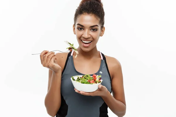 Egészség és Fitness koncepció - gyönyörű amerikai afrikai hölgy fitness ruházat, diéta, étkezési friss salátával. Elszigetelt fehér background. — Stock Fotó