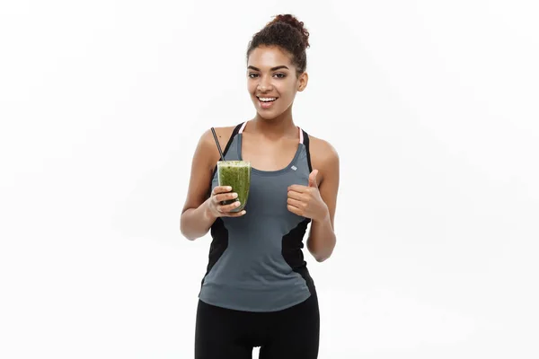 Conceito saudável e Fitness - Linda senhora africana americana em roupas de fitness bebendo bebida vegetal saudável. Isolado sobre fundo branco . — Fotografia de Stock