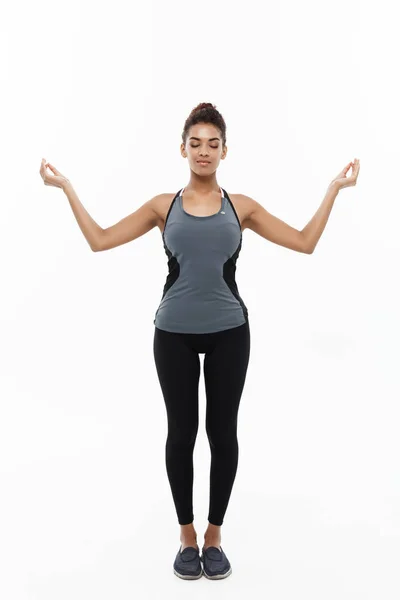 Concepto de salud y fitness - Hermosa dama africana americana en ropa de fitness haciendo yoga y meditación. Aislado sobre fondo blanco . — Foto de Stock