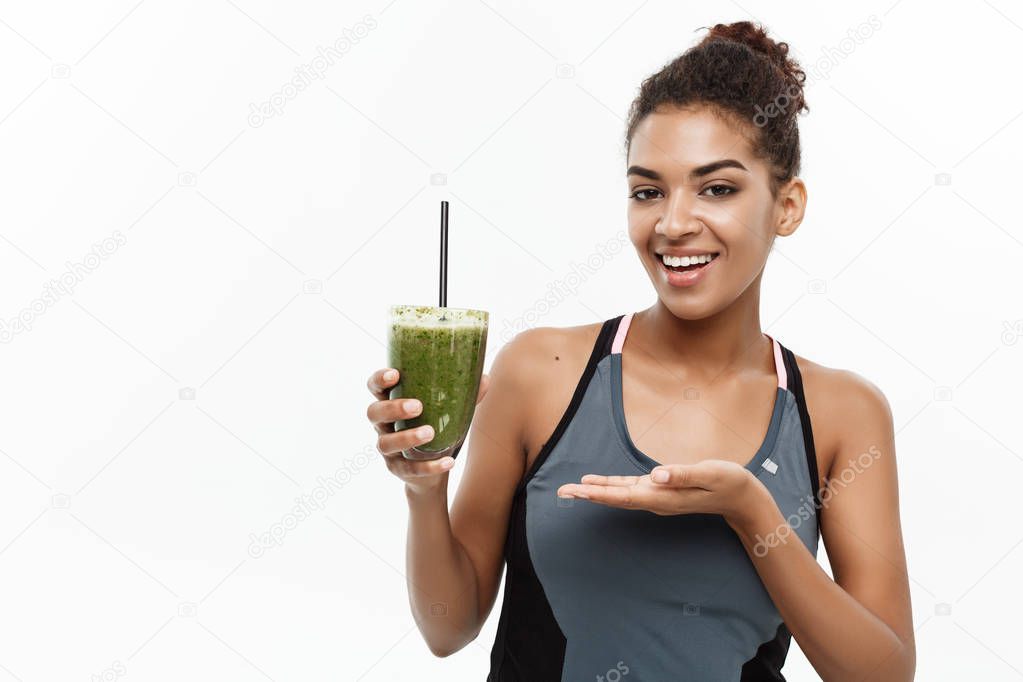 Healthy and Fitness concept - Beautiful American African lady in fitness clothing drinking healthy vegetable drink. Isolated on white background.