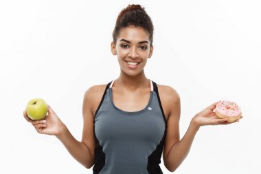Sağlıklı ve diyet kavramı - güzel sportif Afrikalı-Amerikalı çörek ve yeşil elma arasında bir karar olun. Beyaz arka plan üzerinde izole.