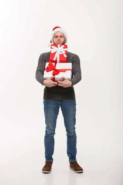 Christmas Concept - молодий красивий чоловік з бородою тримає важкі подарунки з виснаженим виразом обличчя на білому тлі — стокове фото