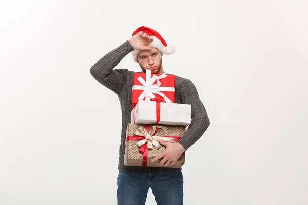 Christmas koncept - ung stilig man med skägg håller tunga presenterar med utmattad ansiktsuttryck på vit bakgrund. — Stockfoto
