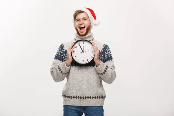 Concepto de vacaciones - Joven hombre barba guapo feliz en suéter sosteniendo reloj blanco sobre fondo de estudio blanco . — Foto de Stock