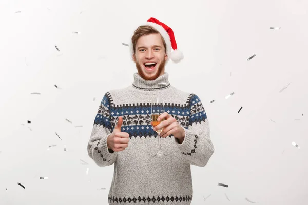 Chirstmas concept - fröhlicher junger kaukasischer Bartträger mit Champagnerglas mit Konfetti-Hintergrund, der Weihnachten feiert. — Stockfoto