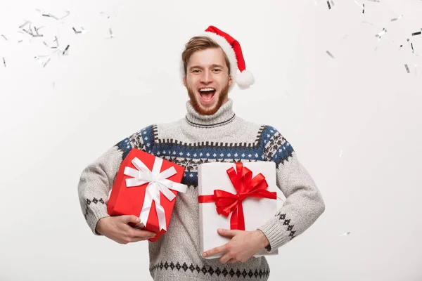 Chirstmas concept - glücklicher junger Mann mit kaukasischem Bart, der eine Geschenkschachtel mit Konfetti-Hintergrund in der Hand hält und Weihnachten feiert. — Stockfoto