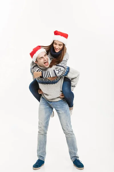 Χριστούγεννα Concept - Full-length νεαρό ζευγάρι ευτυχισμένο σε απολαμβάνοντας piggyback βόλτα που απομονώνονται σε λευκό φόντο γκρι πουλόβερ — Φωτογραφία Αρχείου