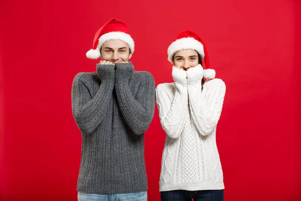 Рождество - портрет улыбающейся пары, которая смотрит в камеру с открытыми глазами на красном студийном фоне — стоковое фото
