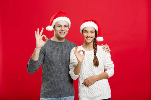 Рождественская концепция - портрет прекрасной молодой пары, показывающей жест ОК пальцем к камере — стоковое фото