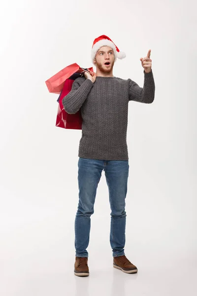Різдвяна концепція - привабливий молодий кавказький чоловік дивує шокуючою торговою сумкою і вказує пальцем попереду . — стокове фото