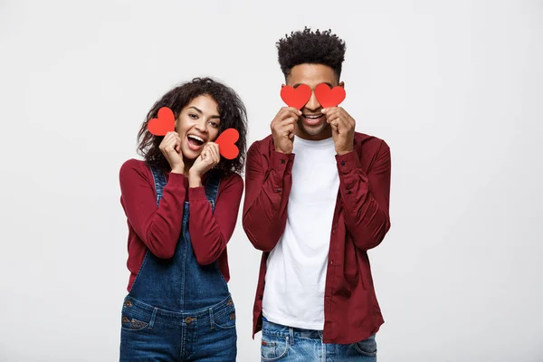 Hermosa pareja afroamericana sosteniendo dos corazones de papel rojo, mirando a la cámara y sonriendo, aislada sobre fondo blanco —  Fotos de Stock