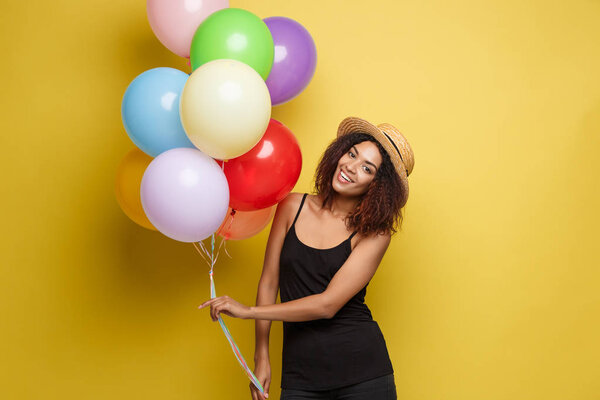 Celebration Concept - Close up Portrait happy young beautiful african woman in black t-shirt smiling with colorful party balloon. Yellow Pastel studio Background