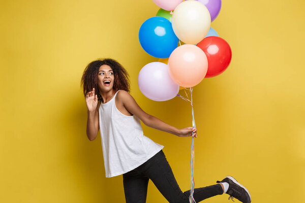 Celebration Concept - Close up Portrait happy young beautiful african woman with white t-shirt running with colorful party balloon. Yellow Pastel studio Background