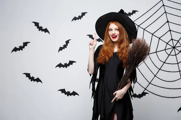 Halloween Concept - Happy elegante heks met bezem halloween wijzende vinger aan kant doen. — Stockfoto