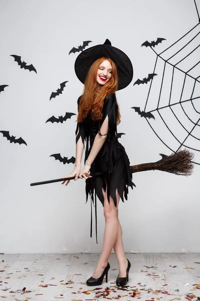 Halloween Concept - Happy elegante heks genieten van het spelen met bezemsteel Halloweenfeest over grijze achtergrond. — Stockfoto