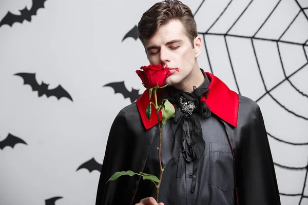 Vampire Halloween Concept - Ritratto di un bel vampiro caucasico con in mano una bella rosa rossa . — Foto Stock