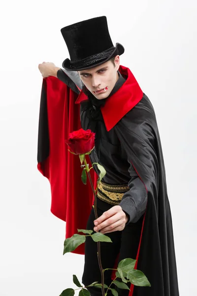 Vampire Halloween Concept - Ritratto di un bel vampiro caucasico con in mano una bella rosa rossa su sfondo bianco . — Foto Stock