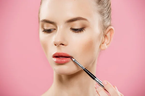 Beauty koncept - žena používat červenou rtěnku s růžové studio pozadí. Krásná dívka dělá make-up. — Stock fotografie