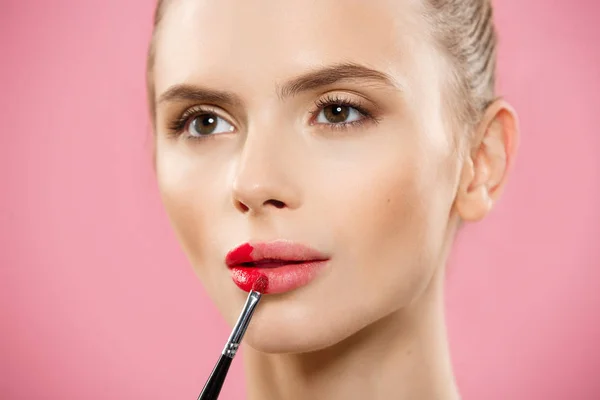 Beauty koncept - žena používat červenou rtěnku s růžové studio pozadí. Krásná dívka dělá make-up. — Stock fotografie