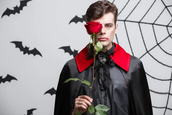 Vampire Halloween Concept - Ritratto di un bel vampiro caucasico con in mano una bella rosa rossa . — Foto Stock