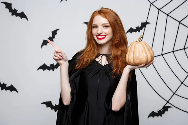 Retrato de una hermosa bruja caucásica sosteniendo calabaza para celebrar Halloween . —  Fotos de Stock