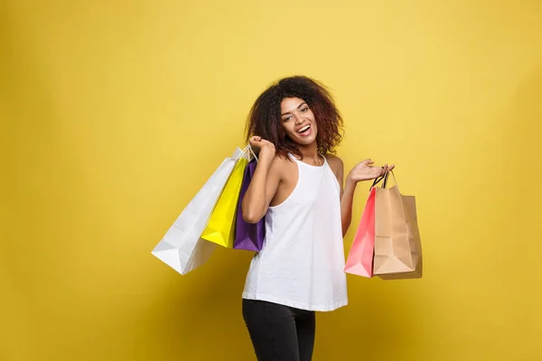 Shopping-Konzept - Nahaufnahme Porträt junge schöne attraktive afrikanische Frau lächelnd und fröhlich mit bunten Einkaufstasche. gelber pastellfarbener Hintergrund. Kopierraum. — Stockfoto