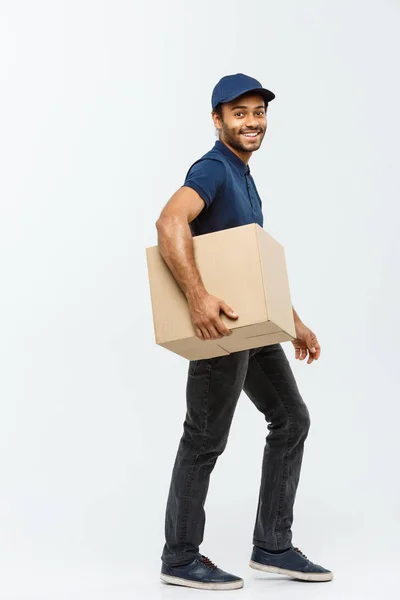 Koncepcja dostawy - portret szczęśliwy African American człowiek dostawy w niebieski tkaniny chodzenie do wysłania pakietu pole do klienta. Na białym tle na studio szary tło. Miejsce. — Zdjęcie stockowe