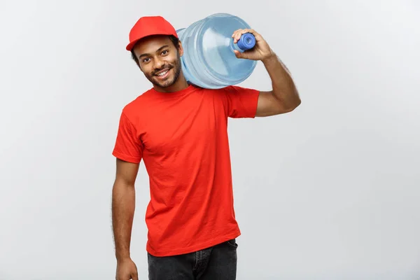 Concetto di consegna - Bello uomo di consegna afroamericano con serbatoio d'acqua. Isolato su sfondo grigio studio. Copia spazio . — Foto Stock