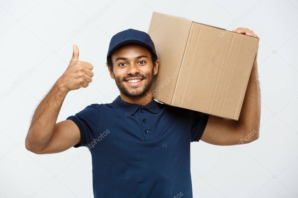 Delivery Concept - Portrait of Happy African American delivery man holding a box package and showing thumps up. Isolated on Grey studio Background. Copy Space.