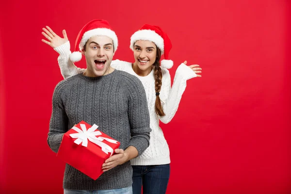 Conceito de Natal - Jovem mulher cobrindo homens olhos com a mão e dando surpresa grande presente. Isolado em fundo vermelho — Fotografia de Stock