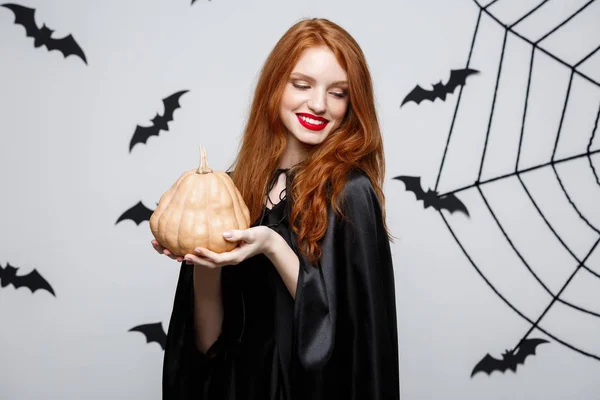 Retrato de una hermosa bruja caucásica sosteniendo calabaza para celebrar Halloween . — Foto de Stock