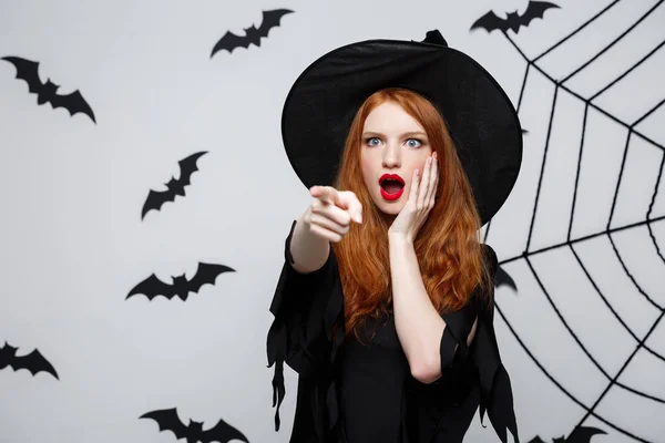 Halloween koncepció - gyönyörű kaukázusi boszorkány sokkoló valami felett szürke háttér. — Stock Fotó