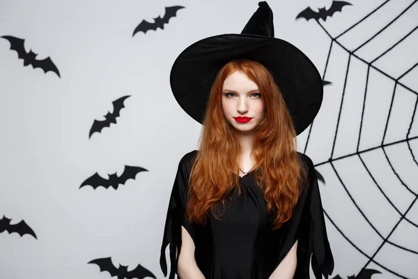 Halloween Concept - mooie ernstige heks met boze gelaatsuitdrukking over grijze achtergrond. — Stockfoto