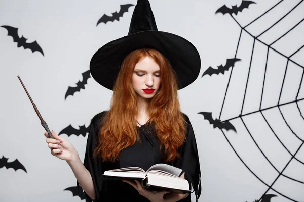 Halloween Concept - Beautiful Witch playing with magic stick on grey background.