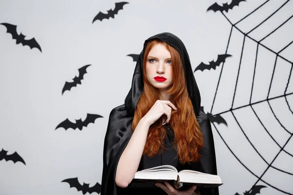 Halloween Concept - Beautiful dark priest casting spell with magic book on grey background. — Stock Photo, Image