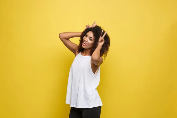 Kul och människor koncept - Headshot porträtt av glad Alfo African American woman med fräknar leende och visar kaninöron med fingrarna över huvudet. Pastellfärgade gula studion bakgrunden. Kopiera utrymme. — Stockfoto