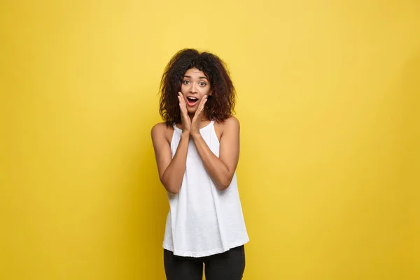 흰색 t-셔츠와 함께 포즈에 아프리카계 미국인 여자 손을 턱에 아름 다운 젊은 미소. 노란 배경에 촬영 스튜디오입니다. 공간 복사. — 스톡 사진