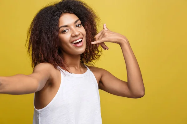 Close-up vrolijke jonge mooie Afrikaanse Amerikaanse vrouw een selfie nemen zichzelf en merk telefoon symbool met de hand. Gele studio achtergrond. Kopiëren van ruimte. — Stockfoto