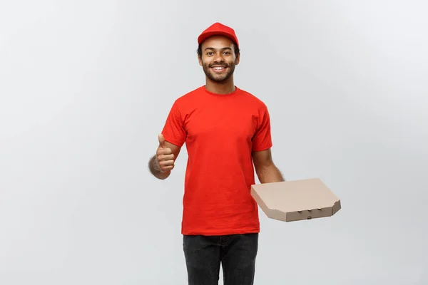 Leverans koncept - porträtt av Happy African American leverans man hålla en pizza låda paket och visar medvetslöshetsattacker. Isolerad på grå studio bakgrund. Kopiera utrymme. — Stockfoto
