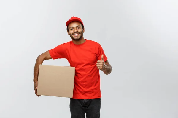 Conceito de entrega - Retrato de homem de entrega afro-americano feliz segurando um pacote de caixa e mostrando thumps para cima. Isolado no estúdio Grey Background. Espaço de cópia . — Fotografia de Stock