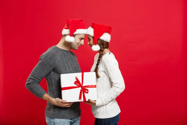 Рождество - одинокая милая молодая пара, крепко держащая белый подарок на красном фоне — стоковое фото