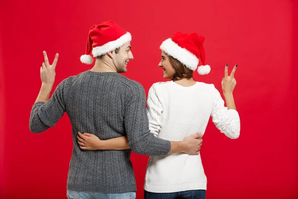 Рождество - обратный вид портрета молодой пары, показывающей жест двумя пальцами — стоковое фото