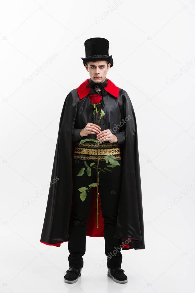 Vampire Halloween Concept - Full length Portrait of handsome caucasian Vampire giving red rose.