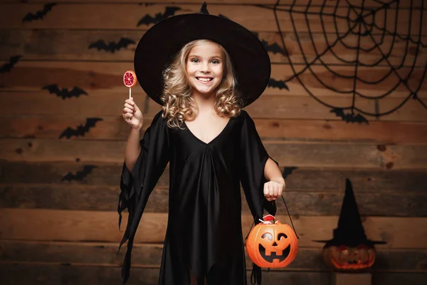 Halloween boszorkány fogalma - gyermek kis boszorkány halloween édes és cukorka-vidám mosolyogva. bat és a spider web háttér felett. — Stock Fotó