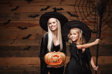 Cadılar Bayramı kavramı - neşeli anne ve kızı cadı kostümleri Cadılar Bayramı ile eğri kabaklar yarasalar ve örümcek ağı ahşap studio arka plan üzerinde poz kutluyor.