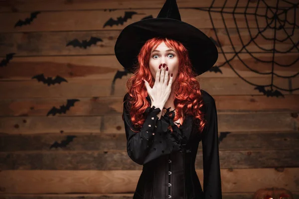 Koncepcja witch halloween - Happy Halloween czerwone włosy czarownica gospodarstwo pozowanie z szoku twarz nad stare drewniane studio tło. — Zdjęcie stockowe